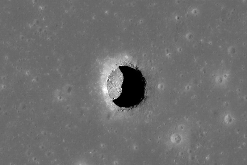 Moon caves: Circular hole in gray lunar landscape, seen from orbit, with bottom visible but partially shaded.