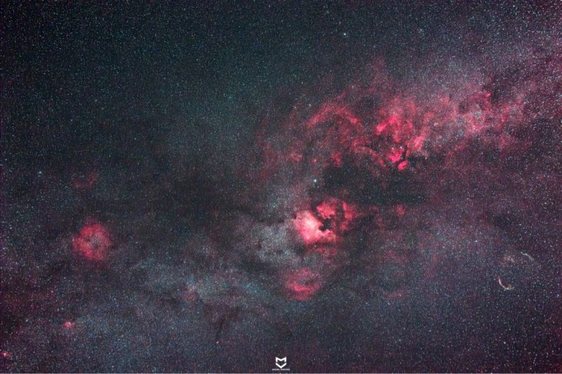Multiple swirls of red nebulosity behind dense but faint star field.