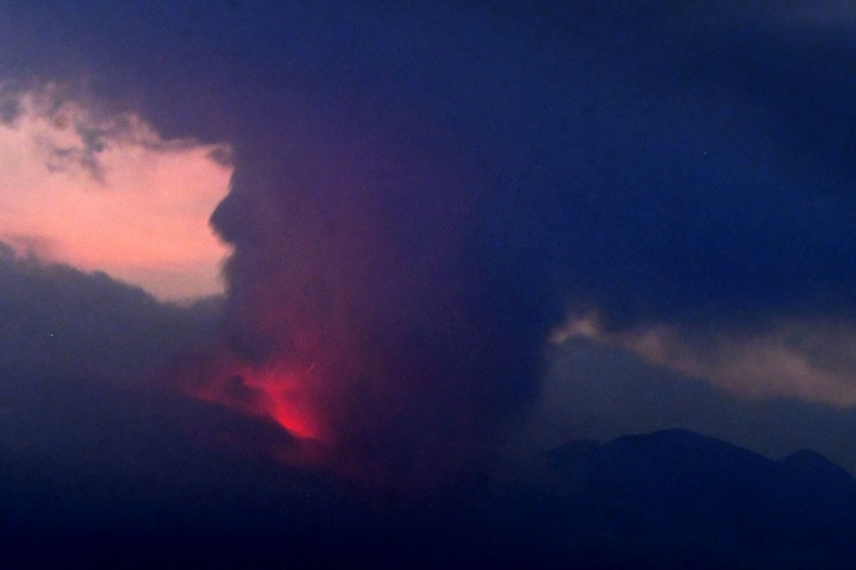 Japan's Sakurajima volcano: Volcano erupting in the dark, with red glow visible under huge cloud of black smoke.