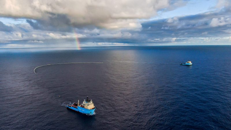 Two ships with a net trailing between them to catch garbage; a rainbow in the background.