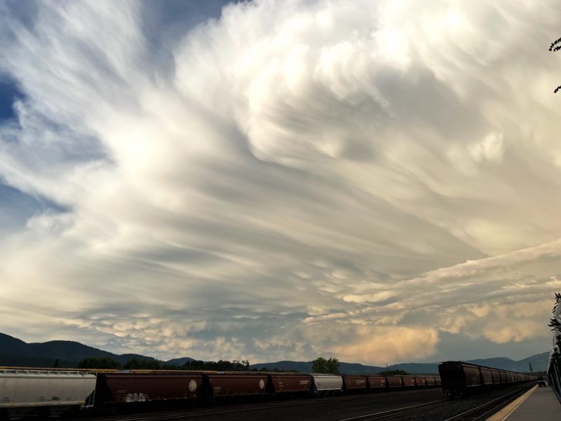 Spreading sheet of white clouds with bumpy spots on underside low and far away, train in foreground.