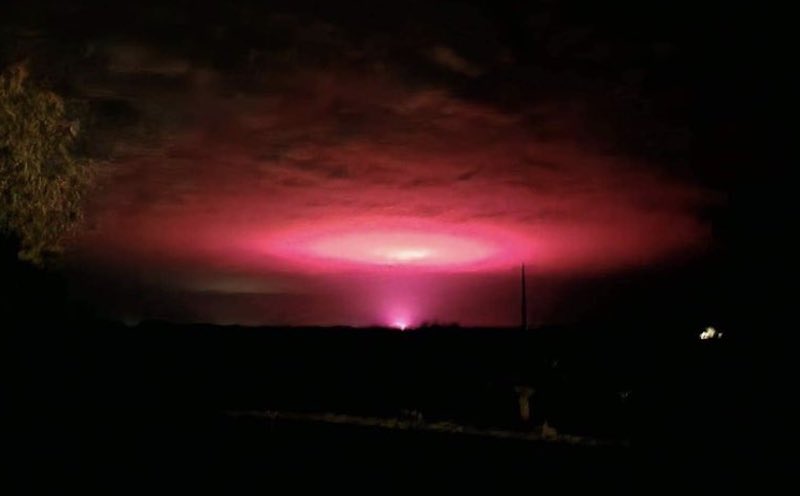Wide mushroom-shaped pink glow in dark sky, apparently reflected from a point source on the ground.