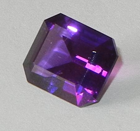 Rectangular faceted purple stone with light refracted from within and gleaming on the surface.