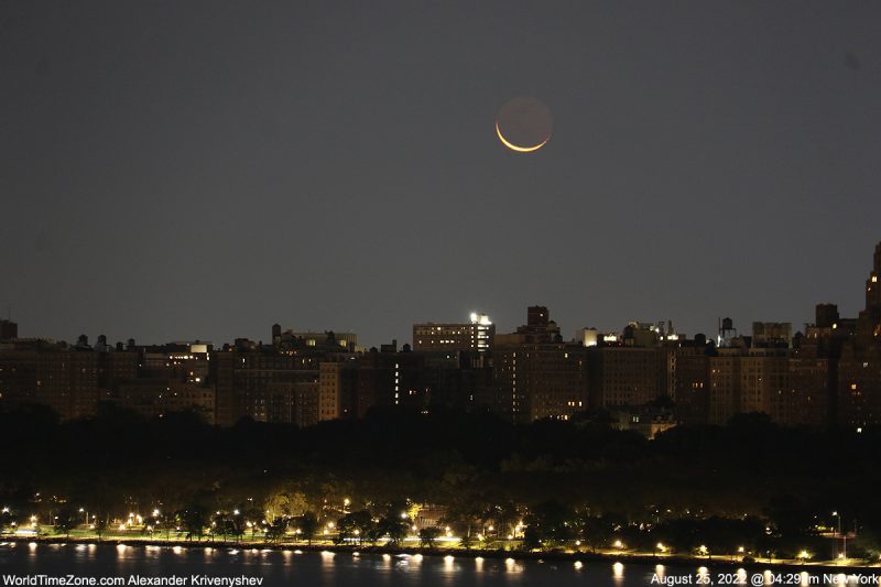 Cityscape in foreground with crescent moon above.
