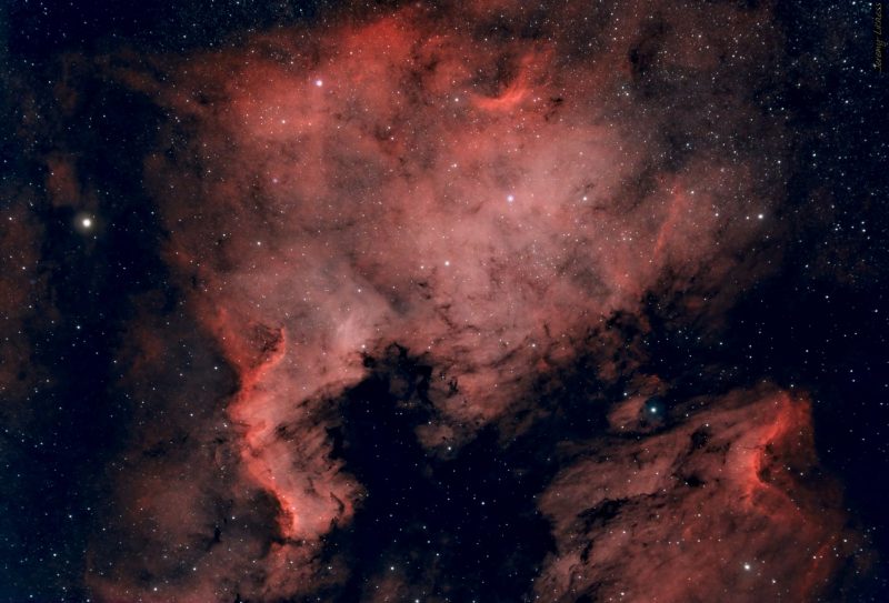 Large clouds of red nebulosity behind a foreground of stars.
