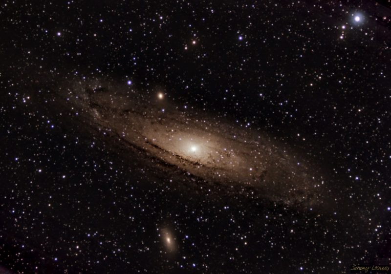 Oblique view of large yellowish spiral galaxy with a multitude of foreground stars.