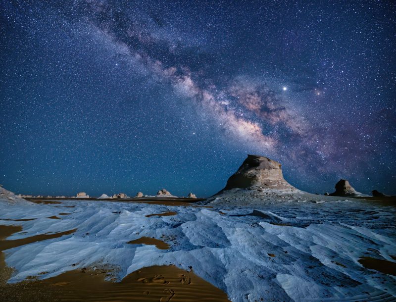 Desert of white wave-like rock, low spires, and Milky Way above.