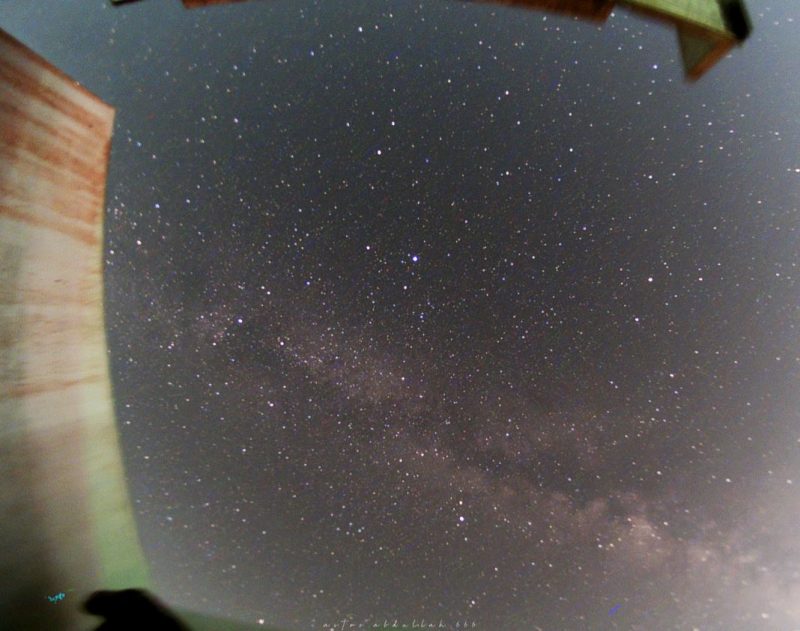 Low clouds of the Milky Way near the horizon, stars throughout, next to a curved wall.