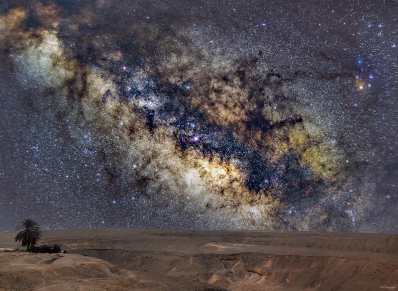Bright and dark colors and a wide, very bright swath of Milky Way over desert.