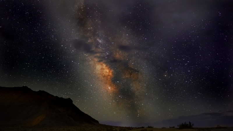 Colorful core of the Milky Way standing tall over the dark landscape.