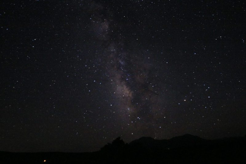 Dark peaks on the horizon and the cloudy Milky Way standing straight up in field of scattered stars.