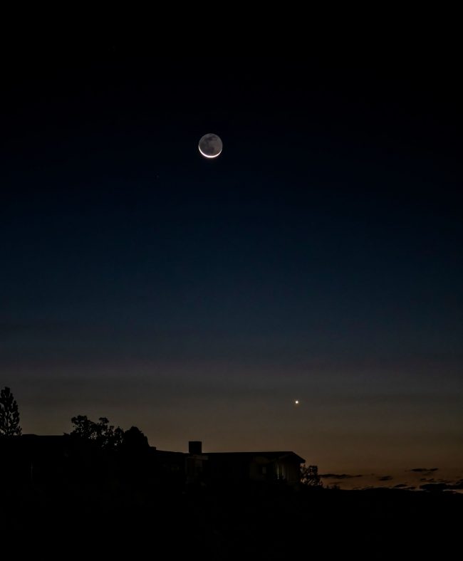 Rooftop in silhouette with dot nearby and crescent moon at top.