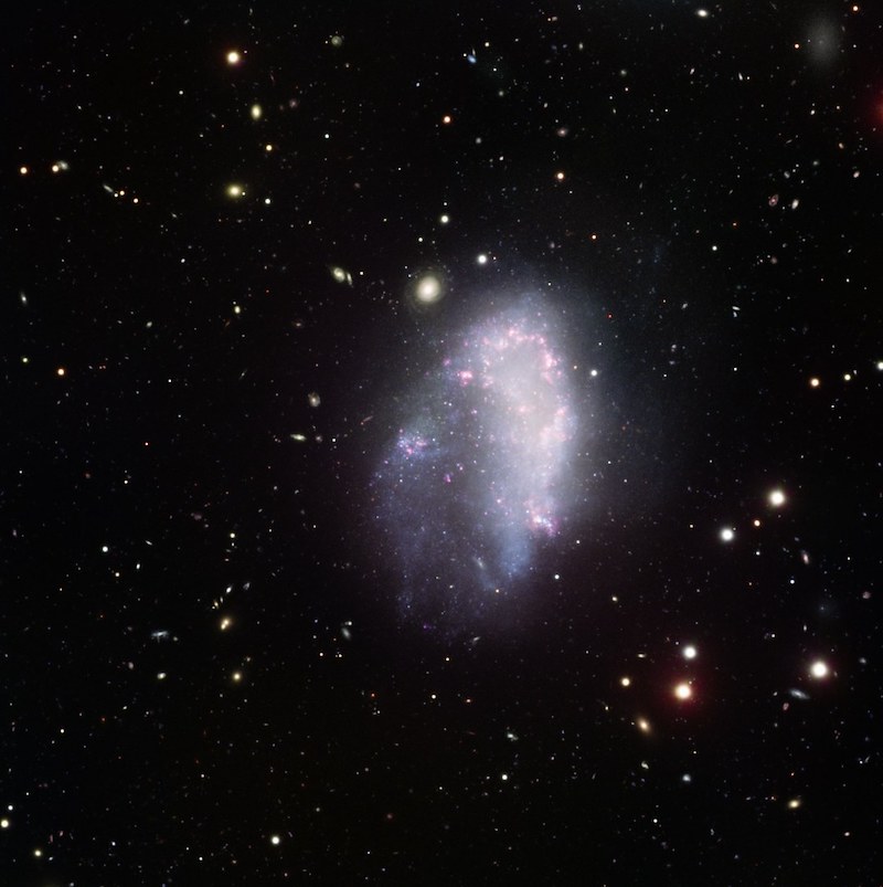 Dark matter halos: Fuzzy-looking galaxy in star field with much smaller and distant galaxies in the background.