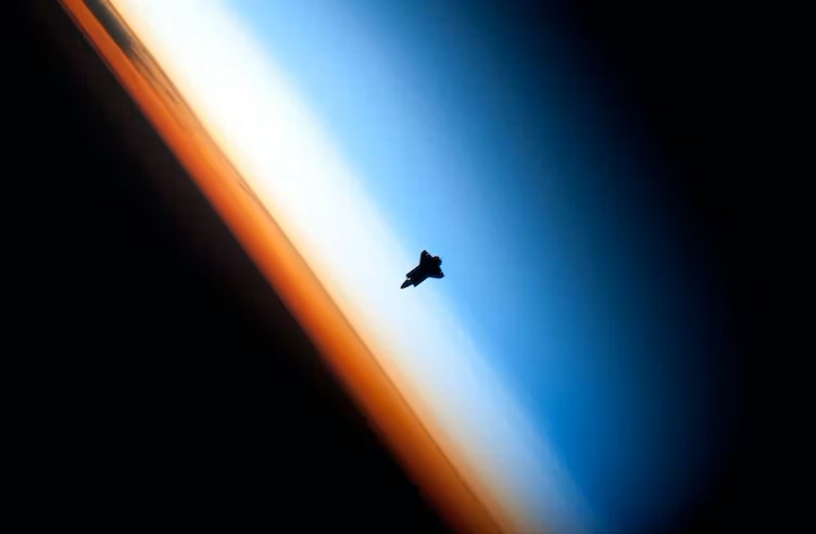 International space laws: Black silhouette of a space shuttle floating over layers of Earth's atmospheric limb and black backdrop of space.