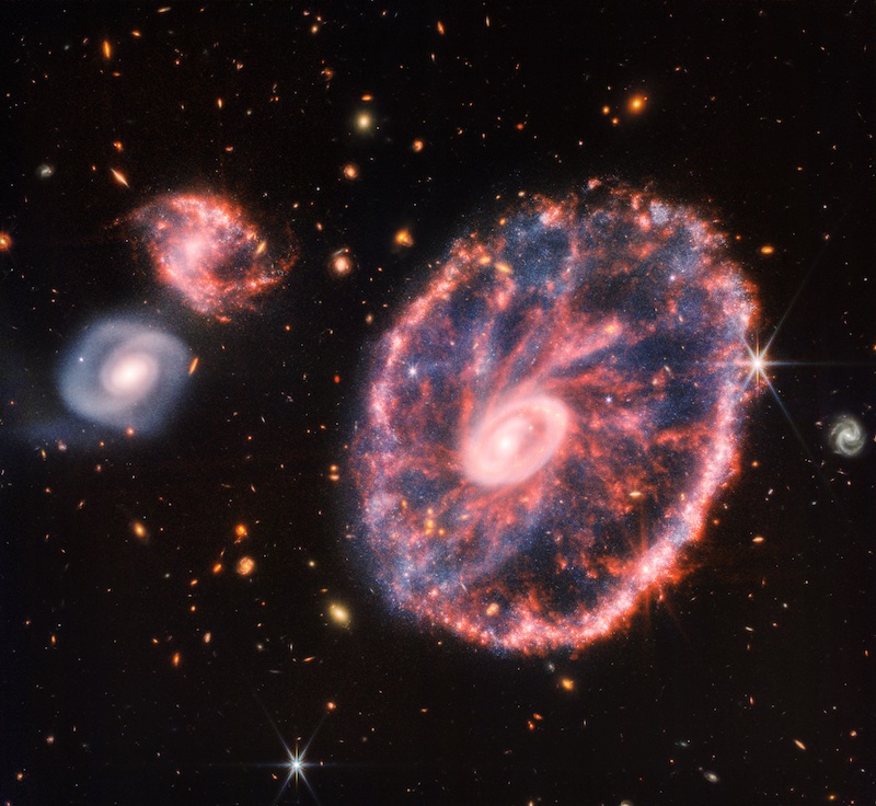 Cartwheel Galaxy: A large oval pink galaxy with many other galaxies from small to large.