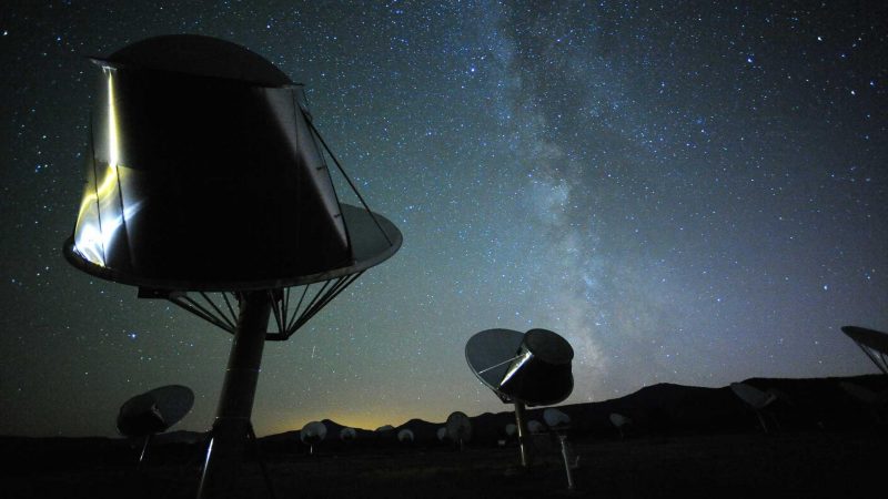 Night sky with Milky Way and telescope dishes in foreground.