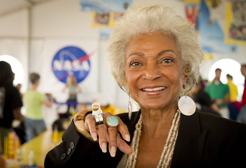 Launches: Woman smiling at camera showing jewelry nasa logo in background.