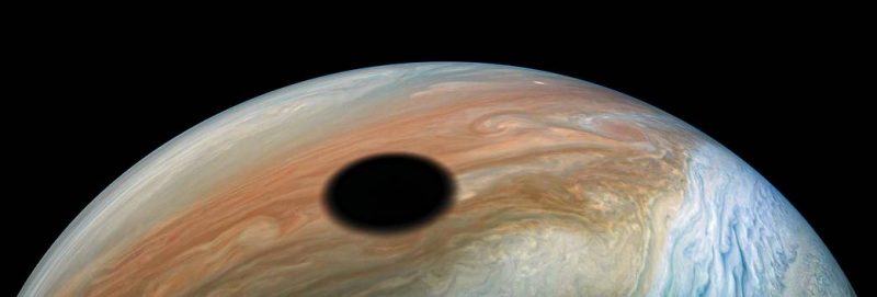 A large, dark, round shadow above a slice of Jupiter's cloudtops.