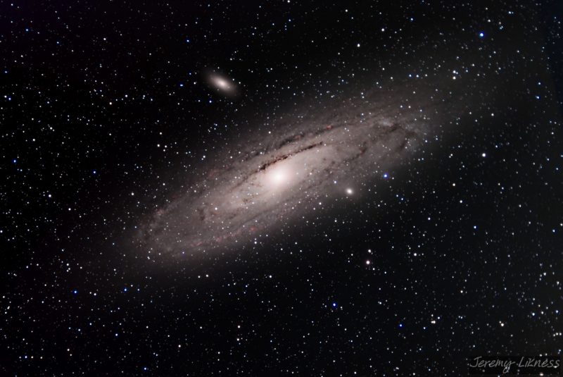 Oblique viewe of large yellowish spiral galaxy with small red patches  and foreground stars.