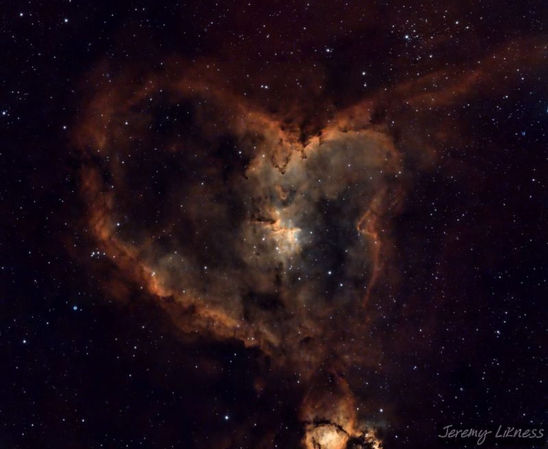 A heart-shaped swirl of orange nebulosity over a background of scattered stars.