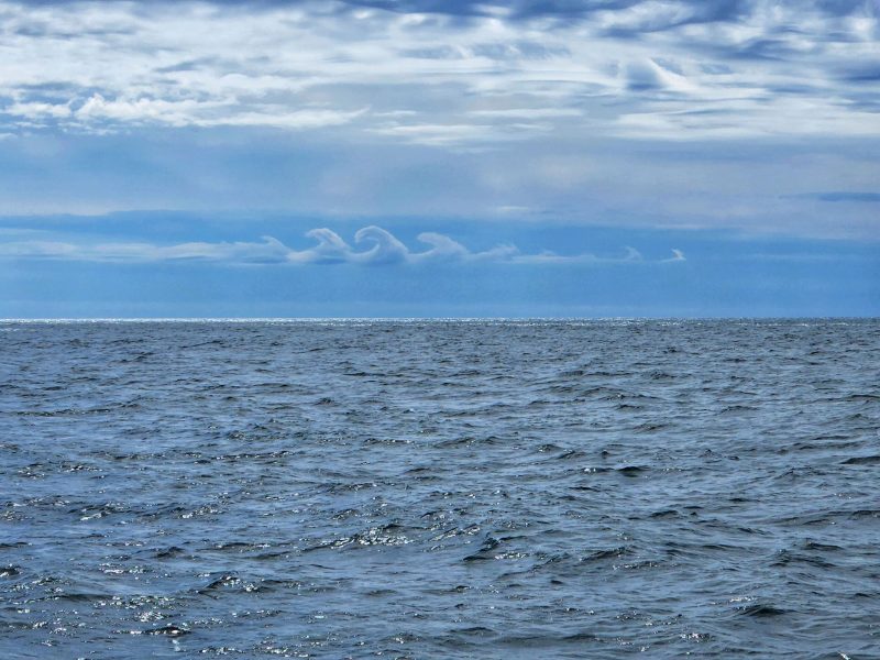 A line of wave-like clouds over the sea.