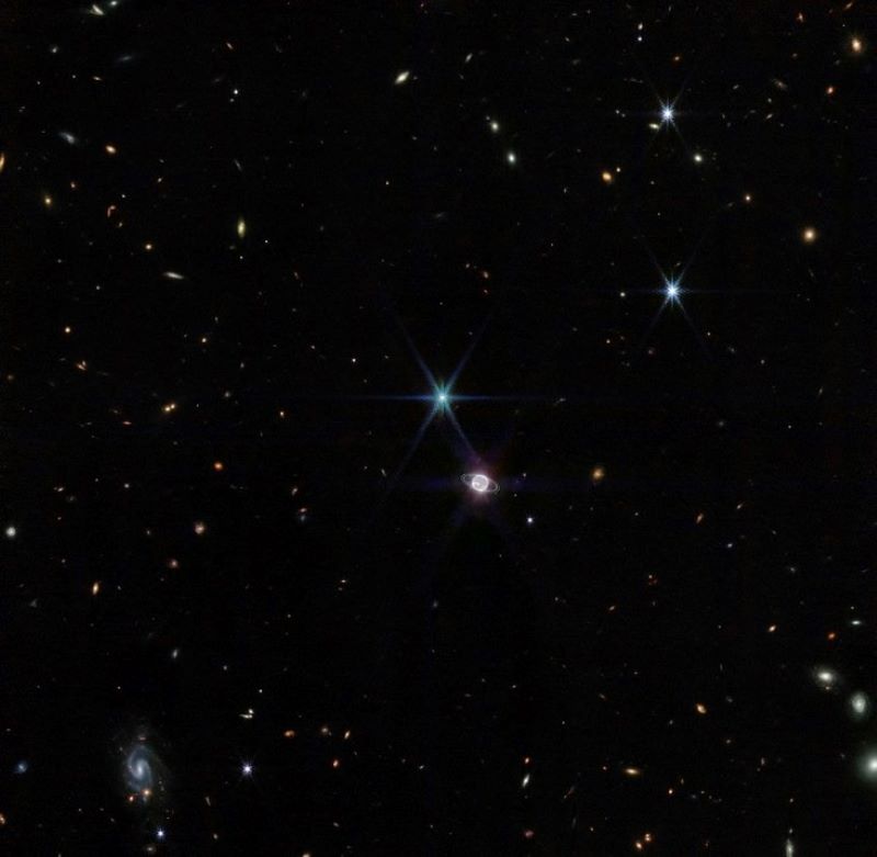 Wide field view showing Neptune and spiky Triton plus small galaxies in the background.