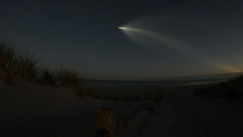 Cigar-shaped light with billowing wispy light behind over dark beach and ocean.