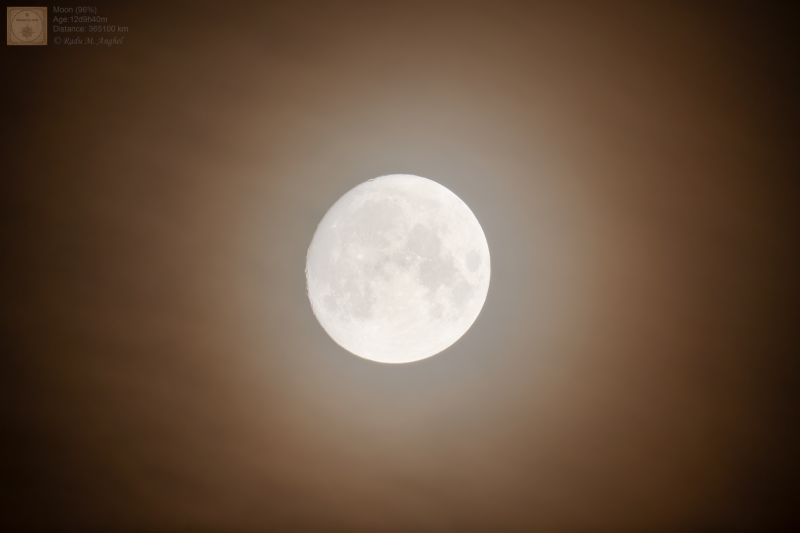 A bright, nearly full moon, with a slight haze in front of it.
