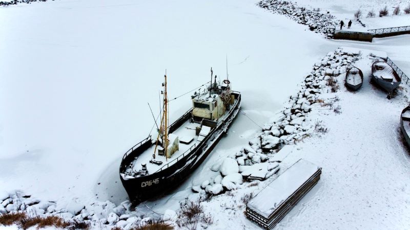 Snowy harbor with snow-covered ship in port.