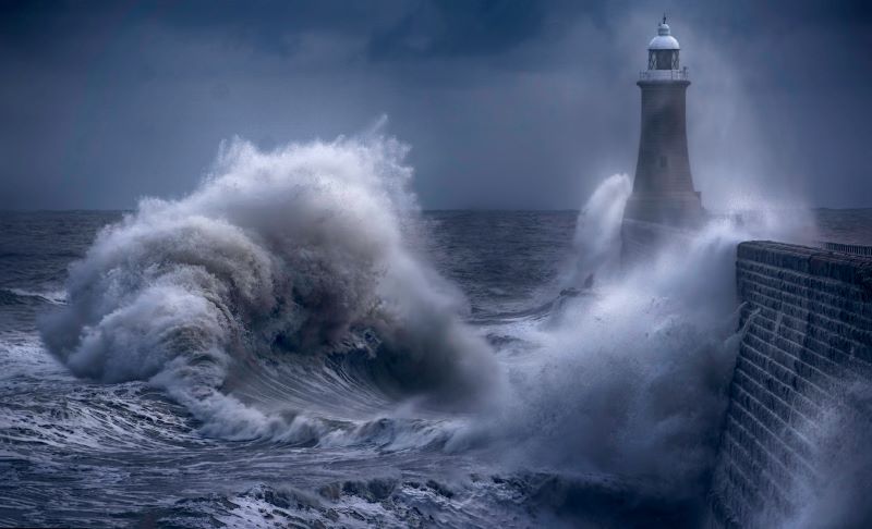 Weather whiplash: A huge wave splashes against a seawall and lighthouse.