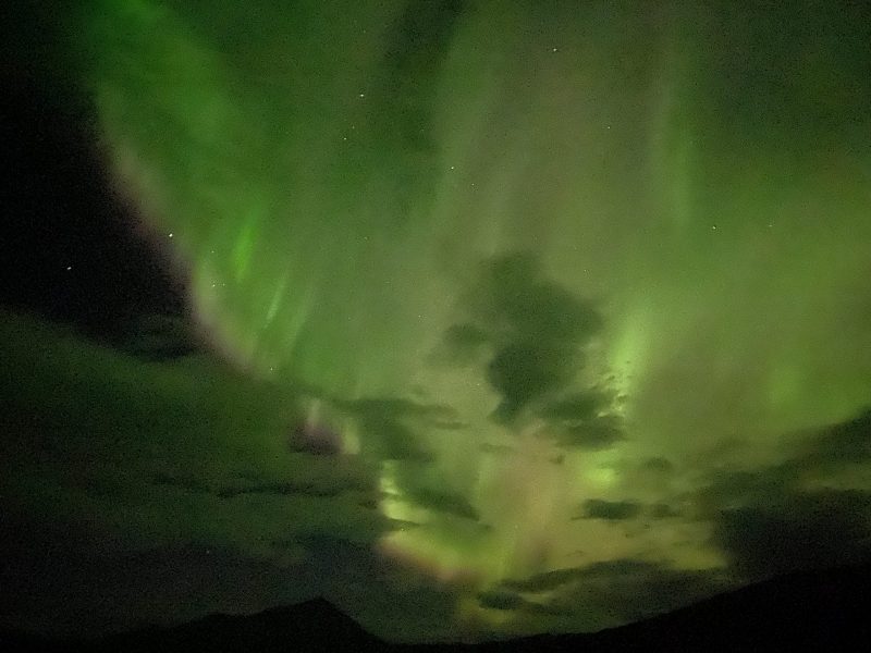 Glowing green swirls and spikes in dark sky above scattered clouds.