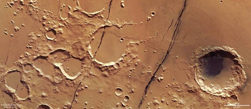 Reddish terrain with craters and 2 long cracks going from top to bottom.