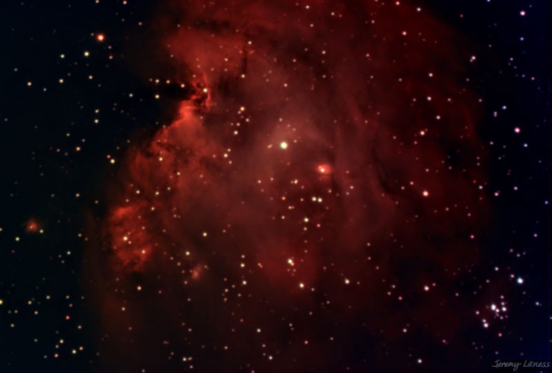 A large, globby red cloud in black space scattered with many stars.