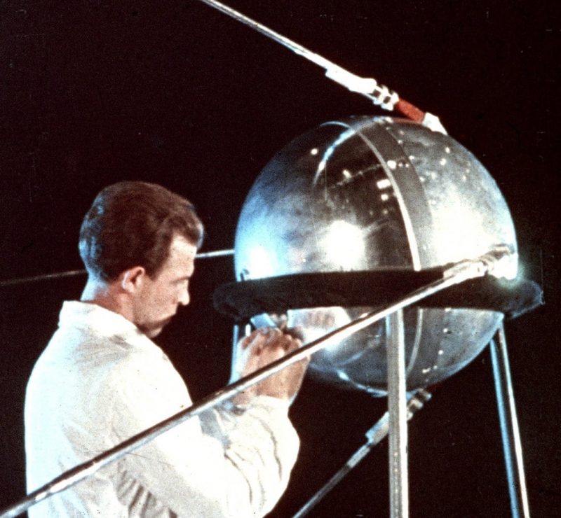 Un ruso con bata blanca trabaja en una gran bola de metal brillante con antenas.