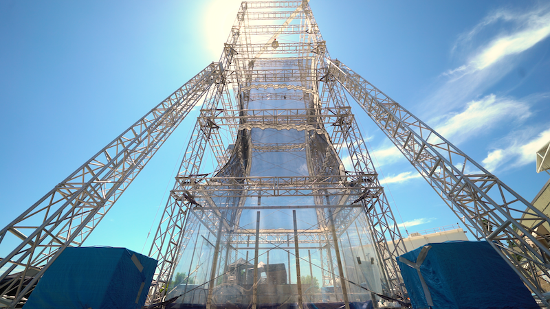 Tall tower made of a grid framework, with blue sky and clouds behind it.