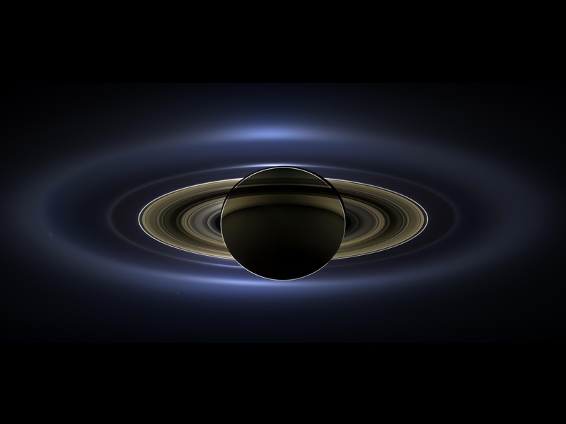 Planet in silhouette with rings and large, translucent blue, fuzzy outer ring.