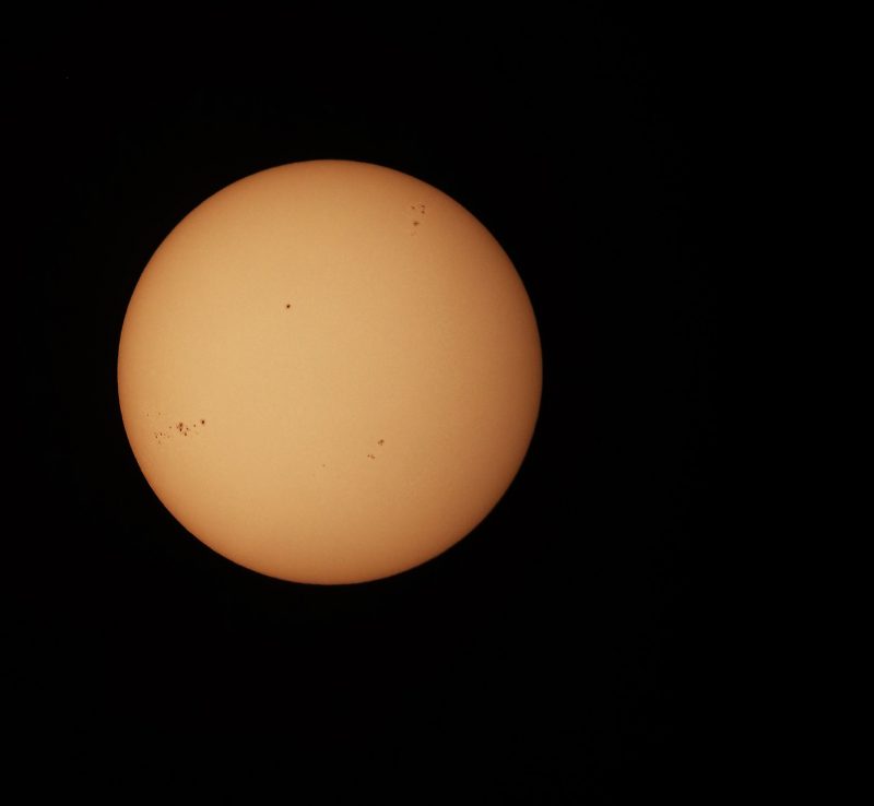 The sun, seen as a yellow sphere with small dark spots.