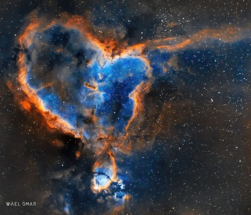 Heart-shaped, light blue cloud with orange rim over a background of distant stars.