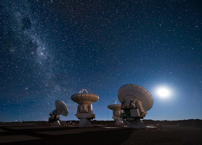 Life beyond Earth: Four dish-shaped radio telescopes pointing to dark blue sky full of stars.