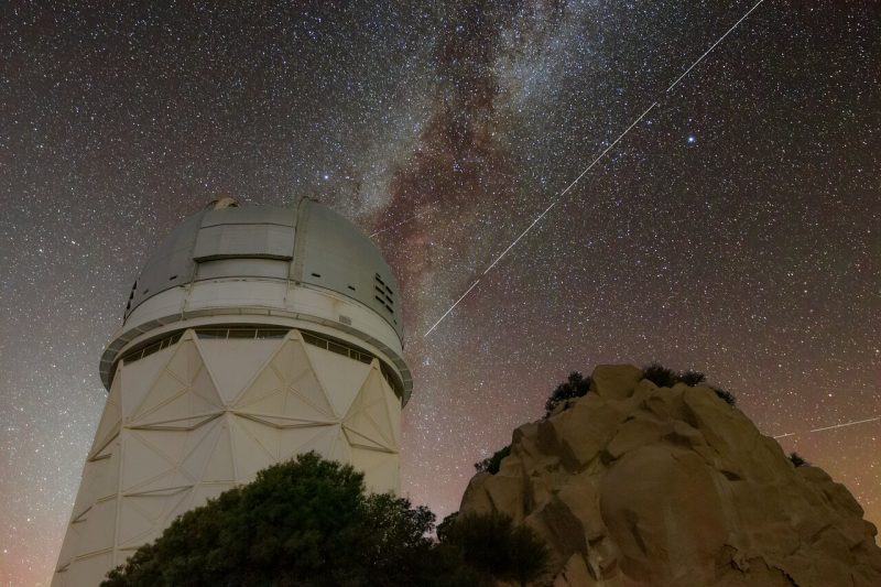 Telescope dome with Milky Way in background and long bright line of BlueWalker 3 in front.