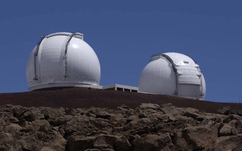 2 white telescope domes with rocky area in the foreground.