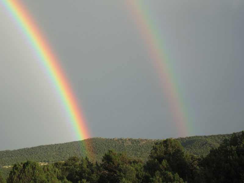 Climate change: Double rainbow over forested hilltops.
