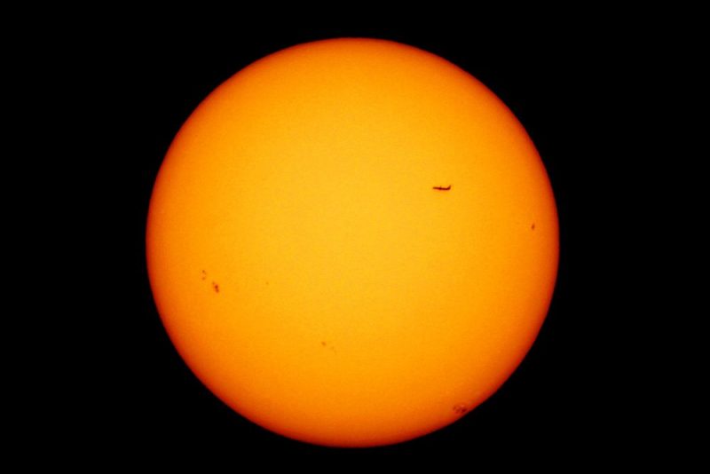 Sun with sunspots and outline of a plane flying in front.