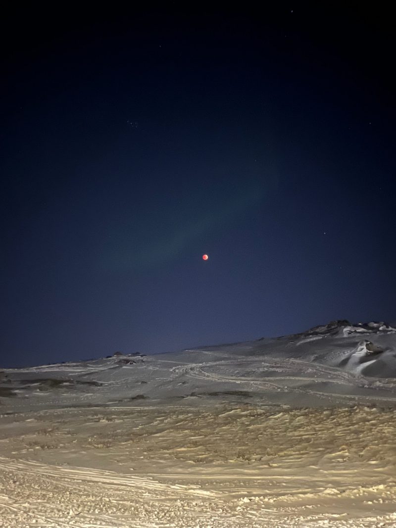 Lunar eclipse in the sky, with a stark, snowy landscape below.