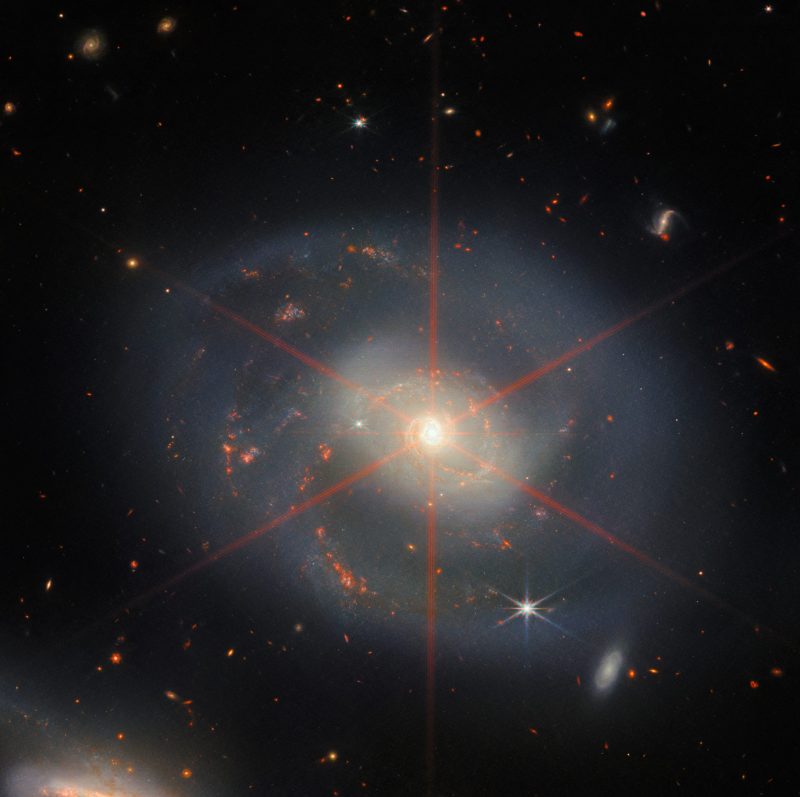 Wreath of star formation: A spiral galaxy with red spiky star lines through the center and some red clumps in arms.