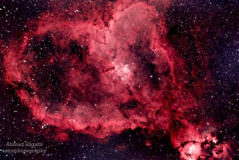 A heart-shaped swirl of reddish nebulosity over a background of distant stars.