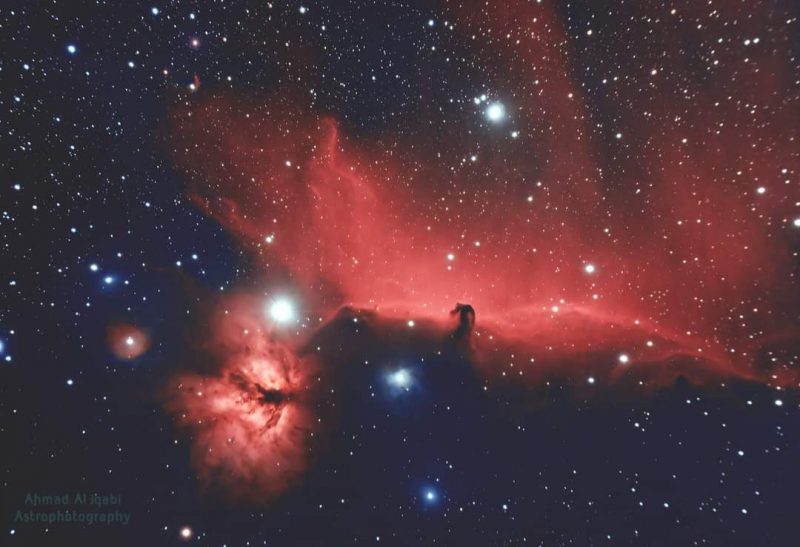 Large, bright reddish clouds of gas over a multitude of distant stars.