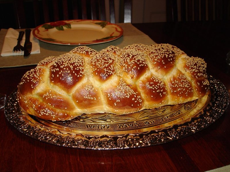 Braided loaf of bread sprinkled with sesame seeds on a platter.