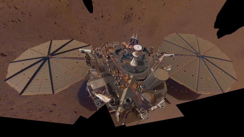 InSight falls silent: Complicated machine sitting on reddish rocky terrain, with 2 umbrella-like dusty solar panels.