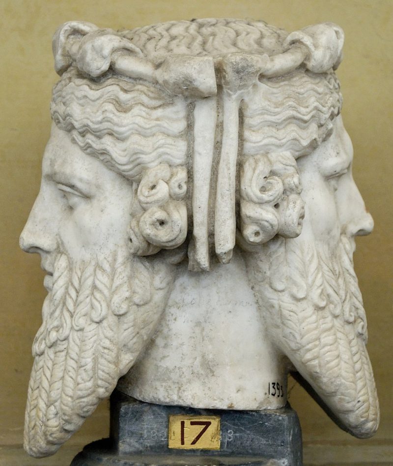 Side view of carved bust with two classical Roman faces back to back, one young, the other old.